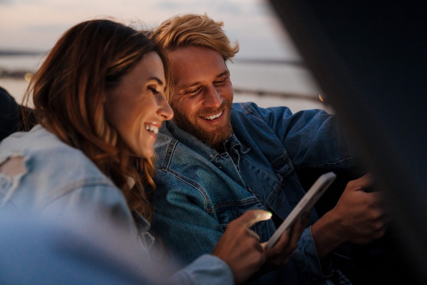 White happy couple smiling and using cellphone during car trip outdoors